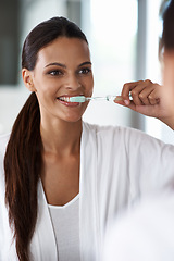 Image showing Woman, brushing teeth and toothbrush for dental, mirror with smile in bathroom for morning routine. Oral hygiene, wellness and orthodontics with toothpaste for fresh breath, health and self care