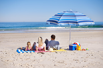 Image showing Family, relax and lying on beach with umbrella for summer holiday, vacation or outdoor weekend together in nature. Rear view of father, mother and daughter chilling on towel or sand by ocean coast