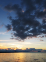 Image showing Ocean, sunset and clouds in sky with mountains, water and seaside in evening. New Zealand, travel and destination for vacation in summer island, landscape and environment for holiday with nature