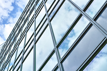 Image showing Low angle, construction and building with glass windows in city for business, office and commercial property with sky. Closeup, architecture and real estate for hotel, accommodation and skyscraper