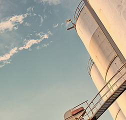 Image showing Closeup, silo and tank at plant for agriculture, bulk storage and product safety with sky, clouds and outdoor. Container, agricultural structure and oil refinery tower with low angle for distillery