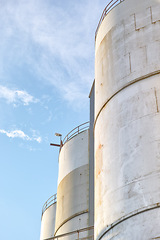 Image showing Closeup, silo and tank at plant for agriculture, bulk storage and product safety with sky, clouds and outdoor. Container, agricultural structure and oil refinery tower with distillery for business