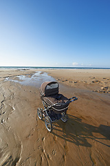 Image showing Stroller, sand and blue sky by beach in nature for travel, vacation or holiday in summer. Baby pram, coast and ocean by seashore for tropical weekend trip on outdoor island destination in Cape town.