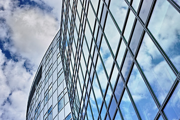 Image showing Low angle, architecture and building with glass windows in city for business, office and commercial property with sky. Clouds, construction and real estate for hotel, accommodation and skyscraper