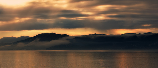Image showing Landscape, silhouette and sea by mountains or sunset background for environment, travel or adventure. Banner of the ocean in nature with clouds, winter and weather by hill in Wellington, New Zealand