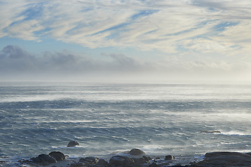 Image showing Clouds, sky and sea with rocks in nature for vacation, holiday or weekend trip in summer. Stones, water and ocean waves by tropical island for travel in Cape town for outdoor paradise scenery.