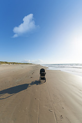 Image showing Stroller, sand and blue sky with cloud by beach for travel, vacation or holiday in summer. Baby pram, nature and ocean by seashore for tropical weekend trip on outdoor island destination in Cape town