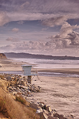 Image showing Beach, landscape and lifeguard tower in summer, morning and travel to island in Norway for vacation or holiday. Ocean, waves and calm water at coast with clouds in sky and mountain on horizon