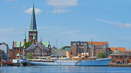 Image showing Harbor, ship and city in nature outdoors, travel and yacht on holiday or vacation or location. Urban, historic building and boat on water for peace or calm in Aarhaus, Denmark and river on getaway