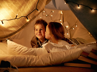 Image showing Children, happy and playing in tent at night with love, kiss and bonding for holiday adventure or vacation. Young boy, girl or kids by fairy lights, pillows and blanket at home with thinking or ideas