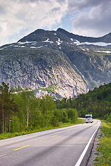 Image showing Mountain, road trip and truck in forest with travel, holiday and countryside scenery in Norway. Nature, clouds in sky and asphalt for journey, vacation or outdoor adventure with snow, trees and woods