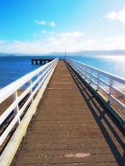 Image showing Mountain, ocean and wooden pier on island with blue sky, tropical landscape and travel in Indonesia. Beach, vacation and relax on wood bridge, jetty or dock with sea water, clouds and summer in Bali