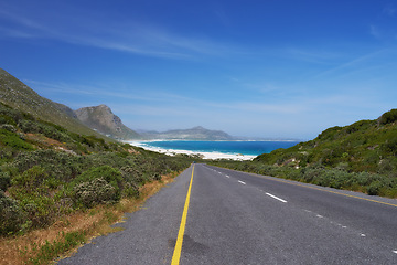 Image showing Mountain, road trip and ocean highway with travel, holiday and countryside scenery in Cape Town. Nature, blue sky and asphalt on journey, vacation and outdoor adventure with beach, horizon and bush