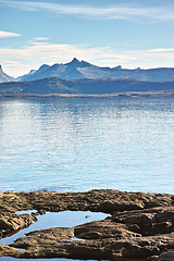 Image showing Lake, landscape and mountains in nature with rocks in Norway on shoreline with ecology for environmental. Water, sea or ocean with hill, stone and outdoor with clouds on horizon for sustainability