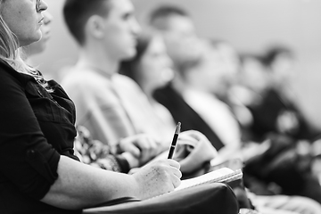 Image showing Female hands holding pen and notebook, making notes at conference lecture. Event participants in conference hall. Black and white image.