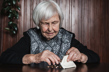 Image showing Portrait of an old woman counting money. The concept of old age, poverty, austerity.