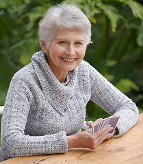 Image showing Senior woman, portrait and outdoors playing cards, happy and game of bridge at park, garden or backyard. Elderly female, smile and poker at table for retirement fun on patio, porch or nursing home