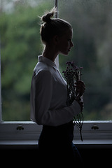Image showing Woman, flowers and window for in home, dark room and mysterious aesthetic for person or artistic pose. Female artist, dim light and silhouette with thinking, fashion and morning setting in dawn