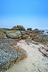 Image showing Rocks, beach and shoreline with blue sky, sunshine and nature with environment and getaway trip. Stones, natural and seaside with fresh air and holiday in South Africa, travel and ocean with sand