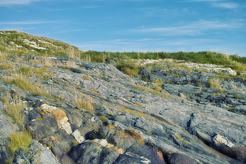 Image showing Mountain, rock and outdoor in bush with grass in nature, environment and landscape with blue sky. Countryside, hill and plants on stone of boulder or travel on rocky trail for hiking or adventure