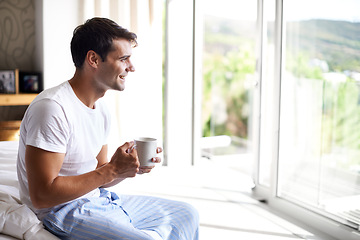 Image showing Man, coffee and bedroom for happiness, smile and cup by window in house at holiday resort. Male person, happy and bed in pajamas or sleepwear for relaxation with tea or latte with drink at home.