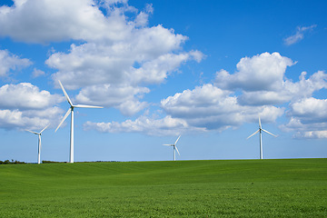 Image showing Clouds, grass and wind turbine for energy, electricity and sustainability in countryside, field and landscape. Blue sky, pasture and windmill for power outdoor in environment, nature and meadow