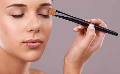 Image showing Face, hand and brush for eyeshadow with woman in studio, makeup and beauty with application on purple background. Cosmetology, transformation and cosmetic care with tools, powder product and shine