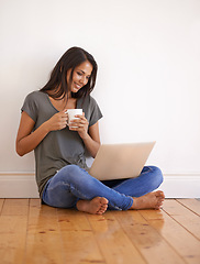 Image showing Apartment, laptop and woman with coffee on floor by wall background in home with smile and mug. Happiness, female person and girl watching movies on site of app online with technology and internet