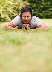 Image showing Music, relax and man on grass in park, streaming sound on headphones for peace or wellness. Nature, audio or radio and happy young person lying on ground for break, rest or sleep in summer with space