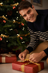 Image showing Portrait, Christmas tree and man wrapping present in home for preparation of holiday event of tradition. Box, gift and smile with happy young person in apartment for December celebration or vacation