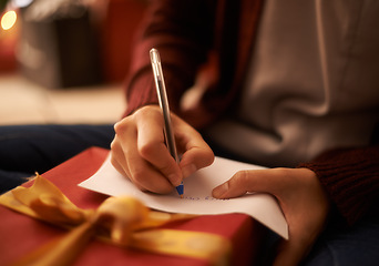 Image showing Hands, writing letter and Christmas in home with box, present and message with festive wish in closeup. Person, pen and paper with notes, gift and package with kindness, celebration and xmas card