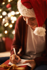 Image showing Woman, writing letter and Christmas with smile by tree, present or santa hat with message for festive wish. Girl, person and paper with notes, gift or package with kindness, celebration and xmas card