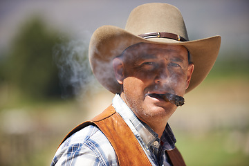 Image showing Portrait, cowboy and man smoking cigar at farm in the rural countryside in Texas. Ranch, face and serious person with tobacco in western hat outdoor, nicotine and casual clothes in nature at stable