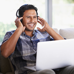 Image showing Man, laptop and living room with headphones, smile and internet for relax and streaming. Indian person, web and tech with house, lounge or apartment for listen to music or podcast with subscription