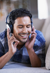 Image showing Man, headphones and listening to podcast on couch, relax and streaming radio for music or sound. Happy male person, home and lying on sofa for peace, comfortable and hearing jazz playlist on weekend