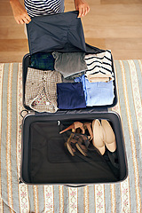 Image showing Hands, travel and person packing suitcase in bedroom of home for holiday or vacation from above. Clothes, getting ready and luggage with tourist bag on bed of apartment, hotel or person for getaway