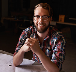 Image showing Portrait, man and architect with documents in workshop on wooden table for paperwork of startup. Confident, entrepreneur and male person with smile for small business in industry for construction