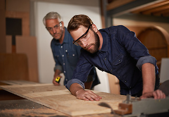 Image showing Carpentry, team and man with wood saw for planning construction project or senior father teaching son. Machine, apprentice and mentor in woodwork, training and serious at workshop with plank on table