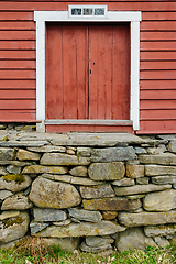 Image showing Vintage red barn door perched on a rustic stone foundation amids