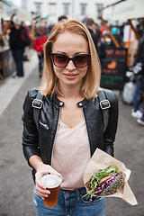 Image showing Beautiful young woman holding delicious organic salmon vegetarian burger and homebrewed IPA beer on open air beer an burger urban street food festival in Ljubljana, Slovenia.