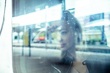 Image showing Woman traveler contemplating outdoor view from window of train. Young lady on commute travel to work sitting in bus or train.