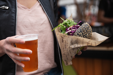 Image showing Close up of woman hands holding delicious organic salmon vegetarian burger and homebrewed IPA beer on open air beer an burger urban street food festival in Ljubljana, Slovenia.