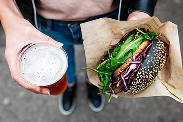 Image showing Close up of woman hands holding delicious organic salmon vegetarian burger and homebrewed IPA beer on open air beer an burger urban street food festival in Ljubljana, Slovenia.