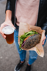 Image showing Close up of woman hands holding delicious organic salmon vegetarian burger and homebrewed IPA beer on open air beer an burger urban street food festival in Ljubljana, Slovenia.