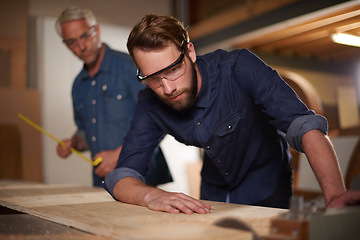 Image showing Carpenter, team and man with wood saw for planning construction project or senior father teaching son. Machine apprentice and mentor in woodwork, training and learning at workshop with plank on table