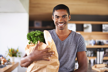 Image showing African man, paper bag and groceries in home kitchen with smile for discount, deal and nutrition choice. Person, shopping and happy in apartment for product, sale and ready with portrait for cooking