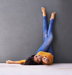 Image showing Woman, smile and wall background for point, feet on wall and relaxing on floor in portrait with fashion. Female person, choice and chill at home for happiness, hey you and wellness in jeans with toes
