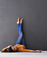 Image showing Woman, style and wall background for laying, feet and relaxing on floor in sleep with fashion. Female person, positive and chill at home for happiness, casual and wellness in jeans with toes in air