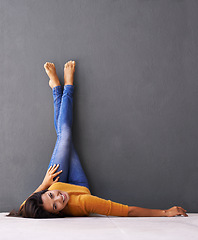 Image showing Woman, smile and wall background, trendy, clothes on wall and relaxing on floor in portrait with fashion. Female person, happy and chill at home for happiness and wellness in jeans upside down