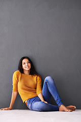 Image showing Portrait, girl and relax or chill on floor with casual outfit for fashion or comfort, leisure and wellness with smile. Female person, isolated with grey background or wall for clothing with mockup.